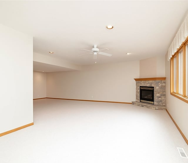 unfurnished living room featuring baseboards, ceiling fan, light colored carpet, a stone fireplace, and recessed lighting