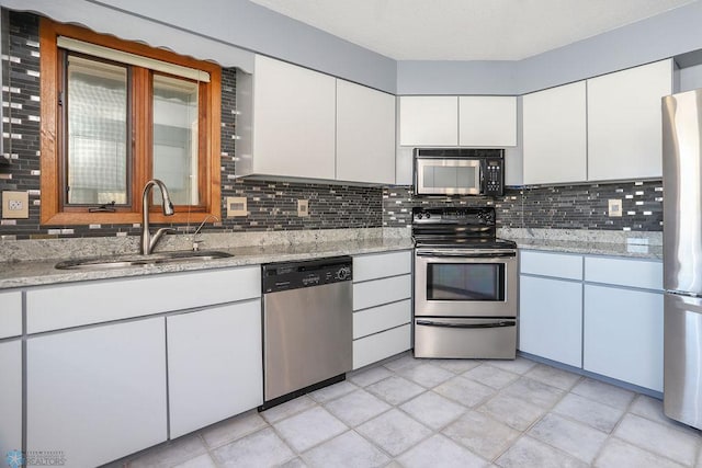 kitchen featuring appliances with stainless steel finishes, a sink, tasteful backsplash, white cabinetry, and light stone counters