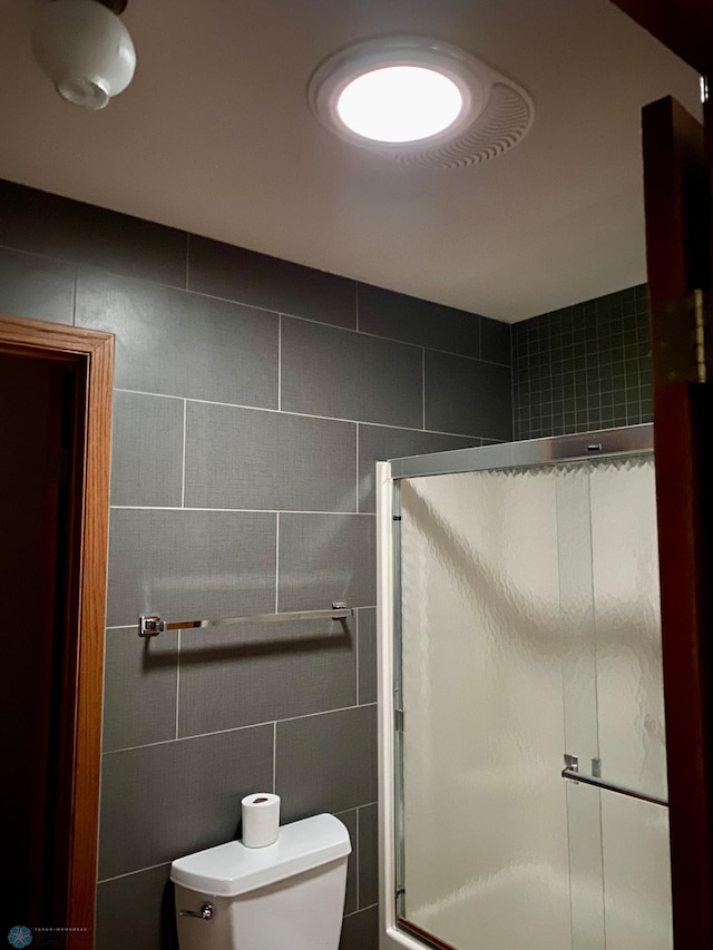 bathroom with a stall shower, toilet, and tile walls