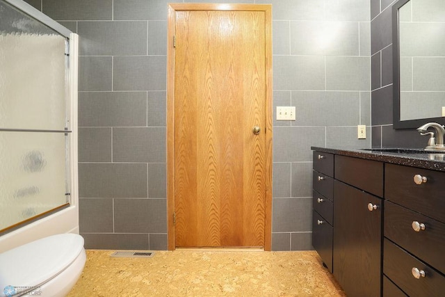bathroom featuring an enclosed shower, vanity, tile walls, and toilet