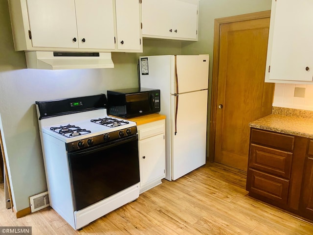 kitchen featuring ventilation hood, gas range oven, black microwave, freestanding refrigerator, and light wood-style floors