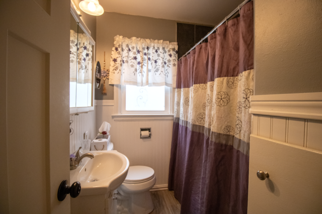 bathroom with toilet, a sink, wainscoting, curtained shower, and wood finished floors