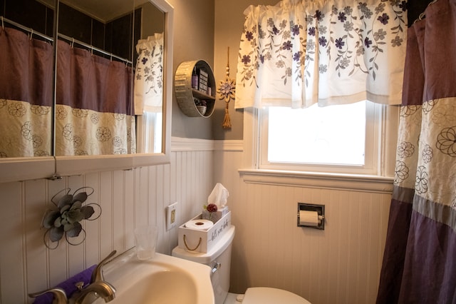 full bath featuring a wainscoted wall, toilet, a shower with curtain, and a sink