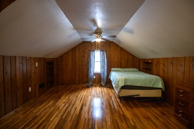 bedroom featuring wood walls, wood finished floors, vaulted ceiling, and a ceiling fan