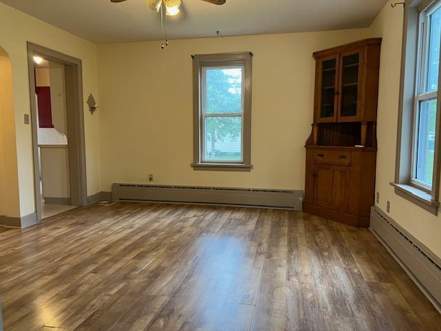 323 Weisel St, Litchfield, MN 55355 - unfurnished living room with baseboard heating, arched walkways, wood finished floors, and ceiling fan