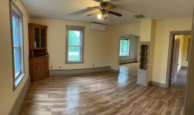 323 Weisel St, Litchfield, MN 55355 - spare room featuring a baseboard heating unit, arched walkways, a wall unit AC, baseboard heating, and wood finished floors