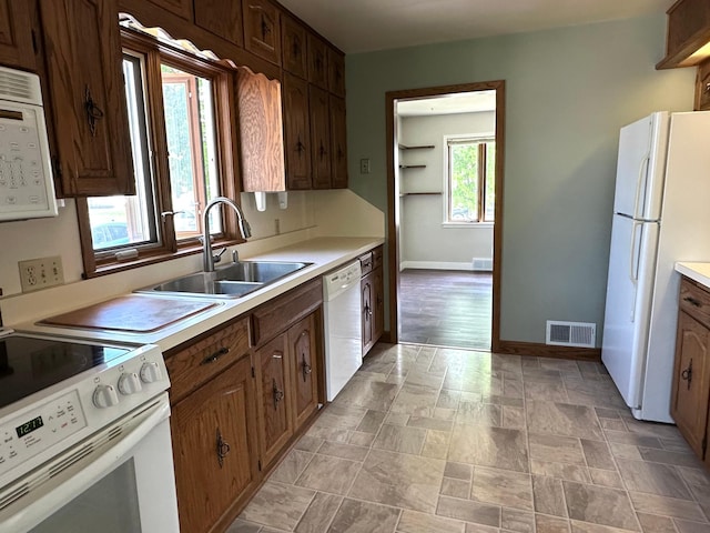 kitchen featuring white appliances, a sink, baseboards, light countertops, and stone finish flooring