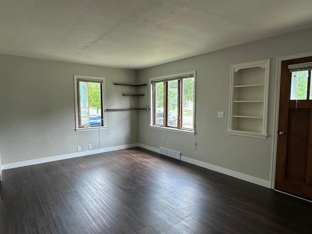 empty room featuring dark wood-style floors, baseboards, and built in features