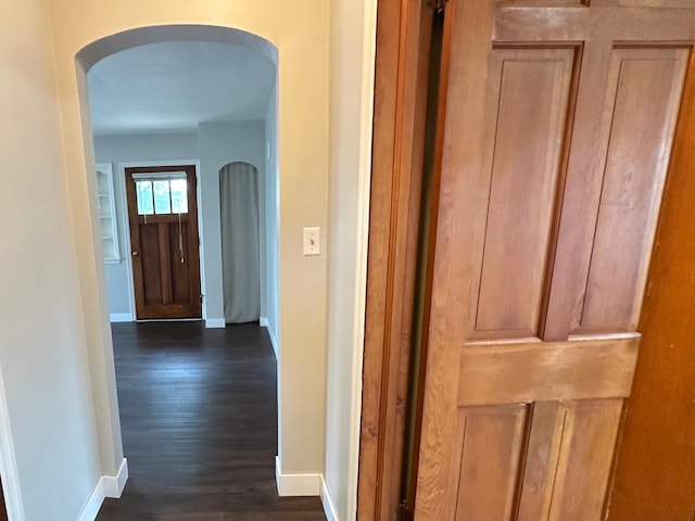 hall with arched walkways, dark wood-type flooring, and baseboards