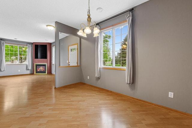 13037 Europa Trail Way N Unit A, Hugo, MN 55038 - unfurnished room with a chandelier, light wood-style floors, baseboards, a glass covered fireplace, and a textured ceiling