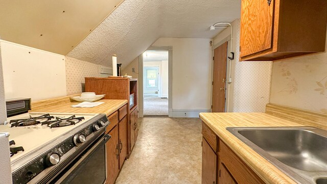 226 3rd Ave NE, Saint Cloud, MN 56304 - kitchen with gas range, brown cabinetry, a textured ceiling, wallpapered walls, and light countertops