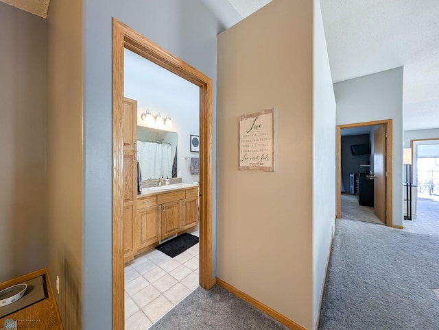 corridor featuring light carpet, a sink, and baseboards