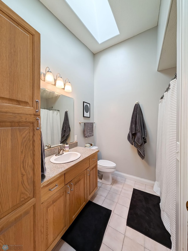 bathroom featuring a skylight, vanity, tile patterned floors, toilet, and baseboards