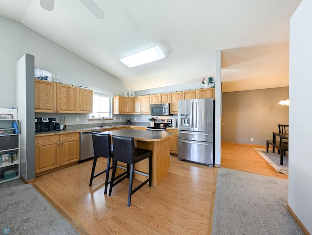 kitchen with stainless steel appliances, lofted ceiling, a sink, light wood-style floors, and a center island