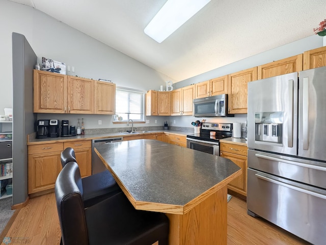 kitchen featuring appliances with stainless steel finishes, a sink, lofted ceiling, light wood-style floors, and a kitchen bar