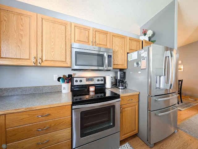 kitchen featuring appliances with stainless steel finishes, lofted ceiling, light wood-style flooring, and light countertops