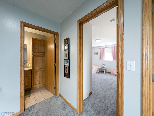 hall featuring light carpet, baseboards, and light tile patterned floors