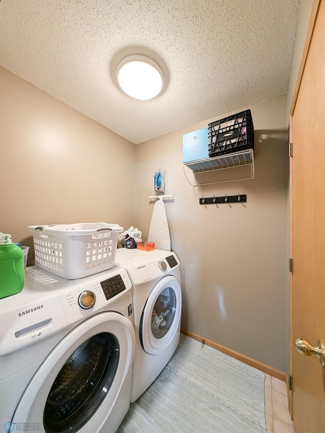 clothes washing area featuring washing machine and clothes dryer, a textured ceiling, light tile patterned floors, and baseboards