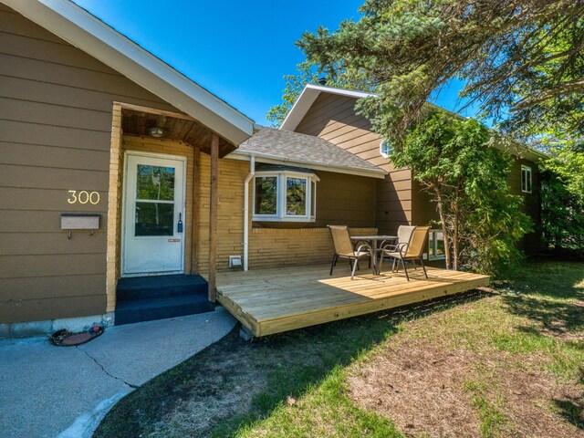 300 27th St NE, Bemidji, MN 56601 - view of exterior entry featuring a wooden deck, brick siding, roof with shingles, and outdoor dining area
