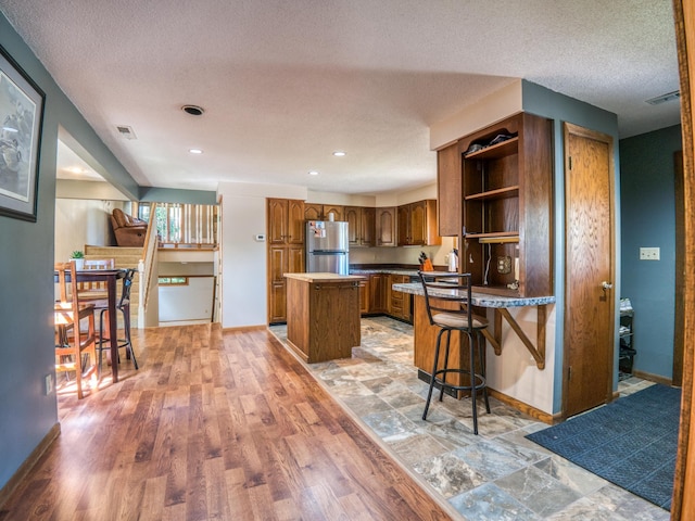 300 27th St NE, Bemidji, MN 56601 - kitchen with freestanding refrigerator, brown cabinetry, open shelves, baseboards, and a textured ceiling