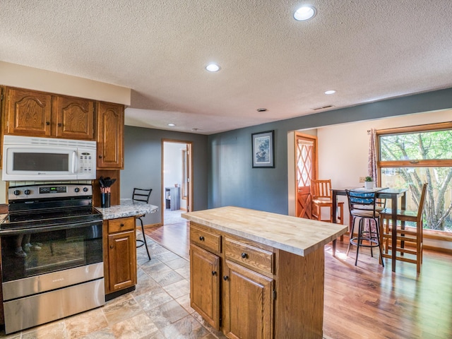 300 27th St NE, Bemidji, MN 56601 - kitchen with stainless steel range with electric stovetop, white microwave, light countertops, a textured ceiling, and brown cabinetry
