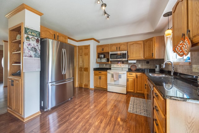 kitchen with appliances with stainless steel finishes, a sink, dark wood finished floors, backsplash, and dark stone counters