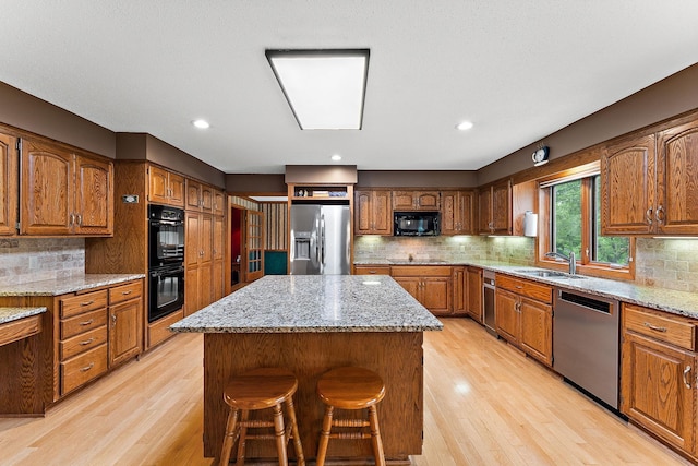 2501 112th St, Bloomington, MN 55431 - kitchen with black appliances, light wood finished floors, a sink, a kitchen island, and brown cabinets