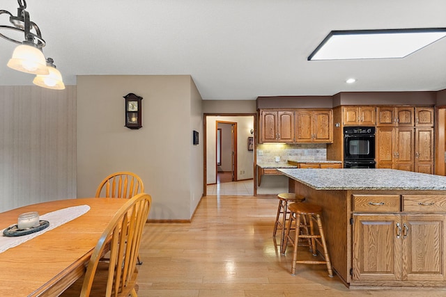 2501 112th St, Bloomington, MN 55431 - kitchen featuring brown cabinets, light wood finished floors, tasteful backsplash, baseboards, and pendant lighting