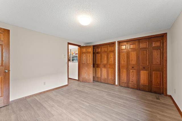 2501 112th St, Bloomington, MN 55431 - unfurnished bedroom with multiple closets, light wood-type flooring, baseboards, and a textured ceiling