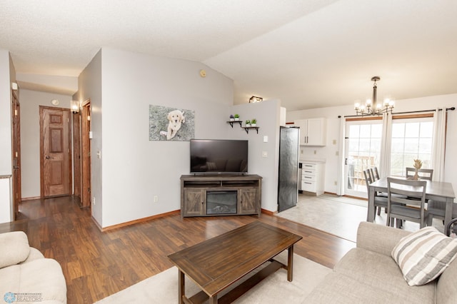 living area with a chandelier, wood finished floors, baseboards, and vaulted ceiling