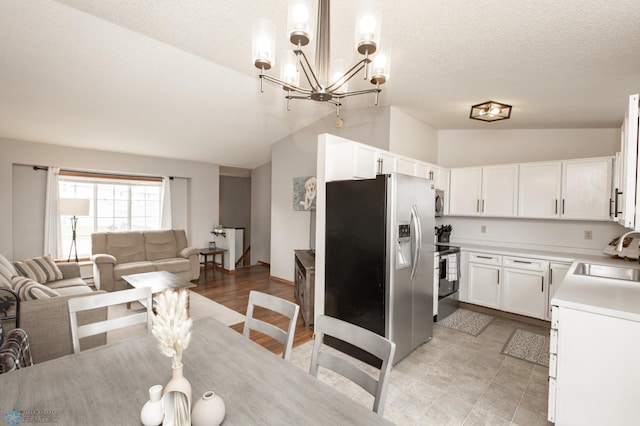 kitchen featuring stainless steel appliances, lofted ceiling, a sink, open floor plan, and white cabinetry
