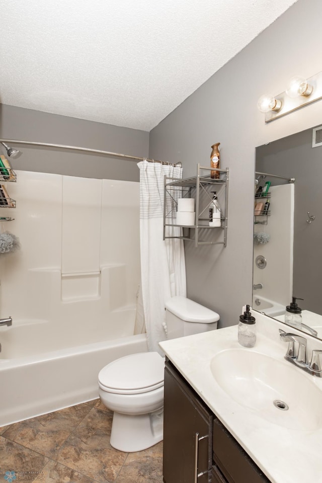 full bath featuring shower / bath combination with curtain, toilet, vanity, stone finish flooring, and a textured ceiling