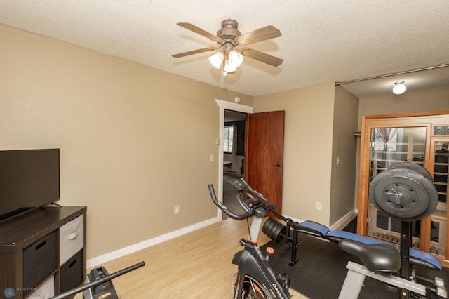 exercise room with ceiling fan, light wood finished floors, baseboards, and a textured ceiling