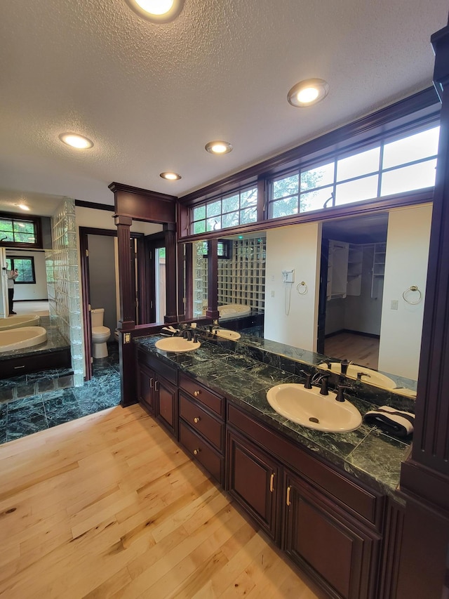 1605 26th St SE, Saint Cloud, MN 56304 - bathroom with wood finished floors, toilet, double vanity, a textured ceiling, and recessed lighting