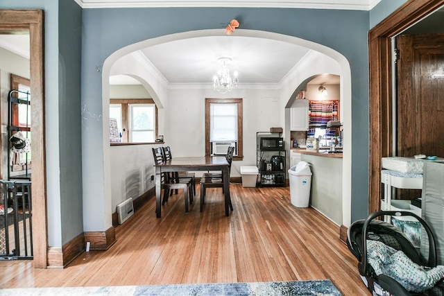 dining space featuring light wood-type flooring, a chandelier, crown molding, baseboards, and cooling unit