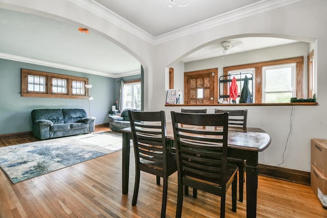 dining room with arched walkways, wood finished floors, baseboards, crown molding, and ceiling fan