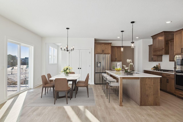 11781 34th St N, Lake Elmo, MN 55042 - kitchen with stainless steel appliances, a sink, light wood-type flooring, an island with sink, and light countertops