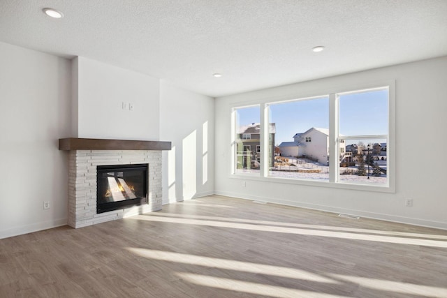 11781 34th St N, Lake Elmo, MN 55042 - unfurnished living room with wood finished floors, a glass covered fireplace, a textured ceiling, baseboards, and recessed lighting