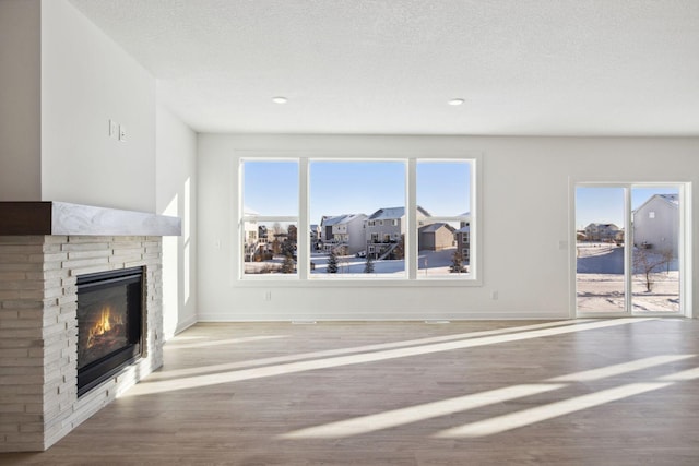 11781 34th St N, Lake Elmo, MN 55042 - unfurnished living room featuring wood finished floors, a glass covered fireplace, plenty of natural light, baseboards, and a textured ceiling