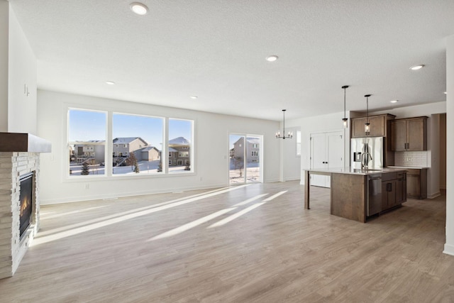 11781 34th St N, Lake Elmo, MN 55042 - kitchen featuring appliances with stainless steel finishes, open floor plan, a fireplace, light wood-style floors, and an island with sink