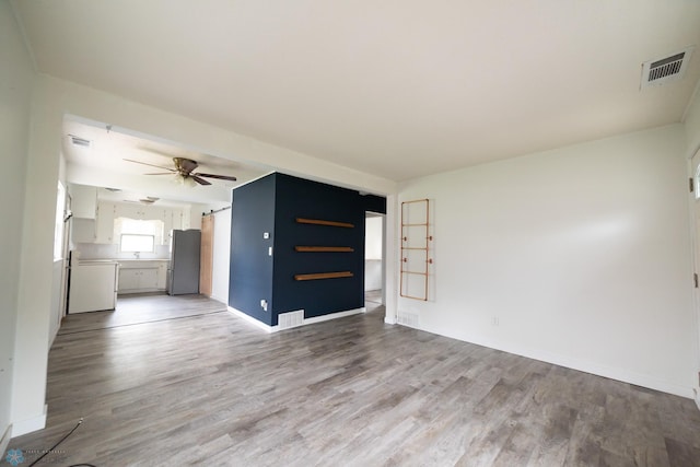 unfurnished living room with light wood-style floors, ceiling fan, baseboards, and a barn door