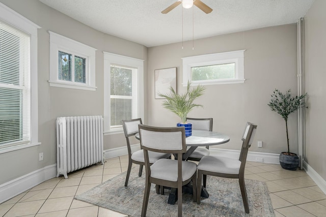 dining area with radiator heating unit, light tile patterned flooring, a textured ceiling, a ceiling fan, and baseboards