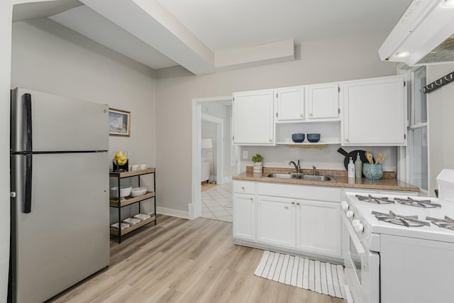kitchen with freestanding refrigerator, a sink, white gas range oven, white cabinetry, and open shelves