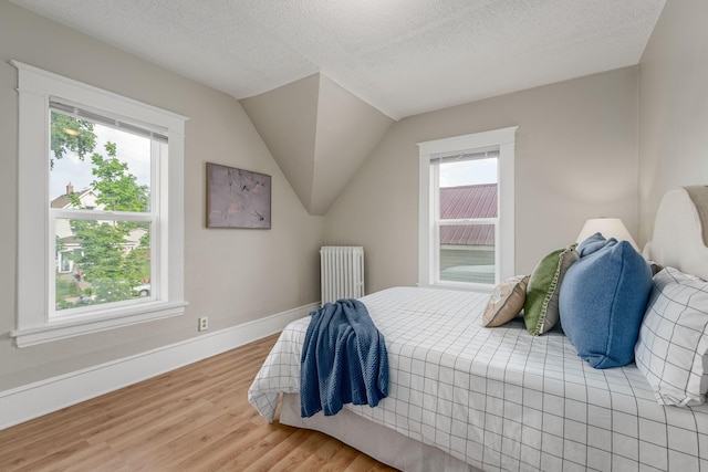 bedroom with radiator heating unit, multiple windows, wood finished floors, a textured ceiling, and baseboards