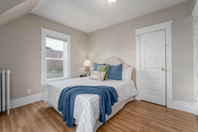 bedroom with radiator heating unit, light wood-style flooring, baseboards, lofted ceiling, and a textured ceiling