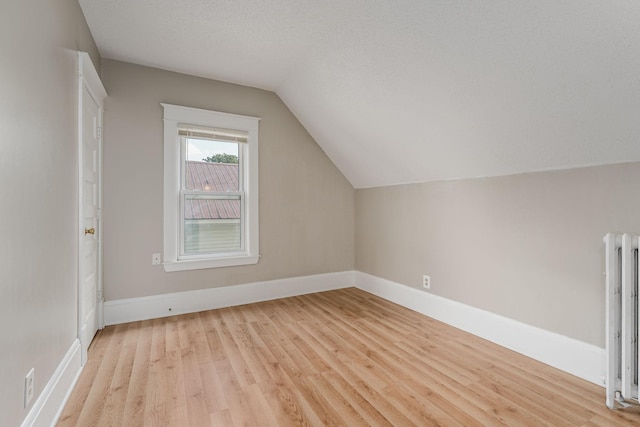 bonus room with radiator heating unit, light wood-type flooring, vaulted ceiling, and baseboards
