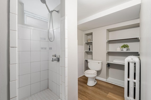 bathroom featuring toilet, a tile shower, radiator, and wood finished floors