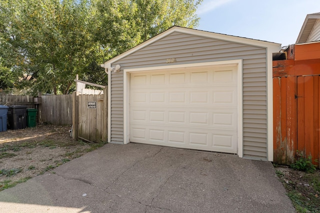 detached garage featuring asphalt driveway and fence