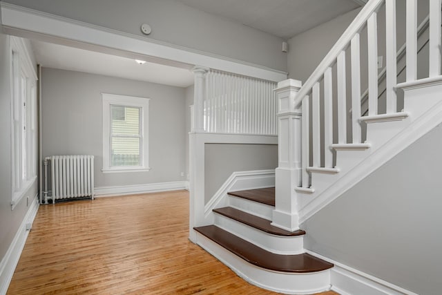 stairway with radiator heating unit, wood finished floors, and baseboards