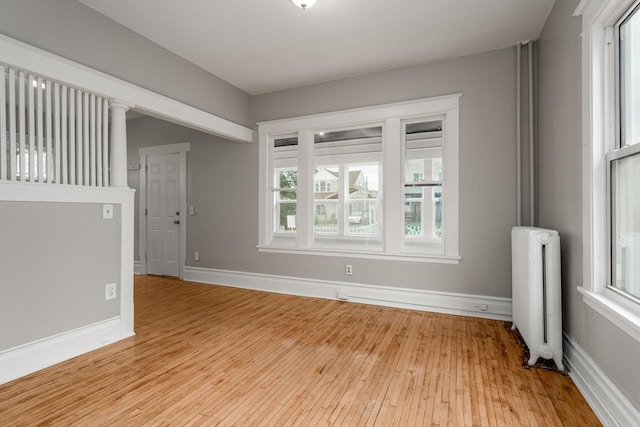 spare room featuring radiator, light wood finished floors, and baseboards